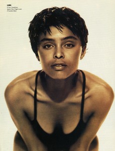 Close-up of a woman with short, textured hair and bold makeup, wearing a black spaghetti strap top.