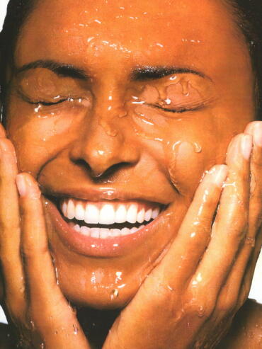 Close-up of a smiling woman with water on her face, eyes closed, hands on cheeks.