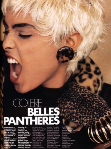 Close-up of a woman with platinum blonde, tousled hair, wearing leopard print accessories and bold makeup.
