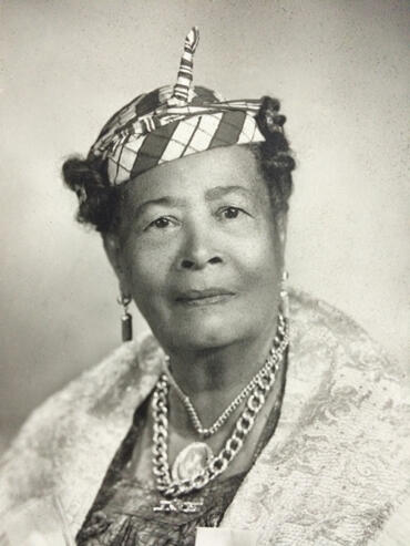 Black-and-white portrait of an elegant woman wearing a patterned headscarf and layered jewelry.