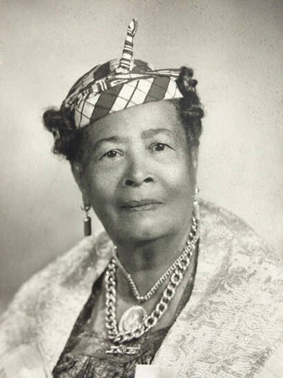 Black-and-white portrait of an elegant woman wearing a patterned headscarf and layered jewelry.