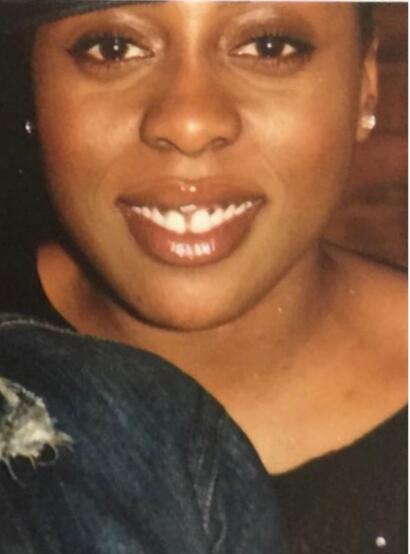 Close-up of a woman smiling, showcasing glossy lips, earrings, and a black top.