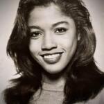 Black-and-white portrait of Susan Monique Horton smiling, with voluminous hair and casual attire.