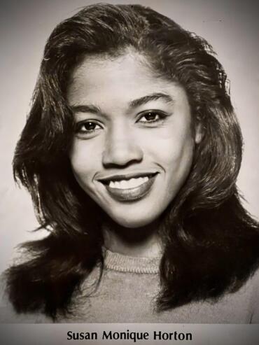 Black-and-white portrait of Susan Monique Horton smiling, with voluminous hair and casual attire.