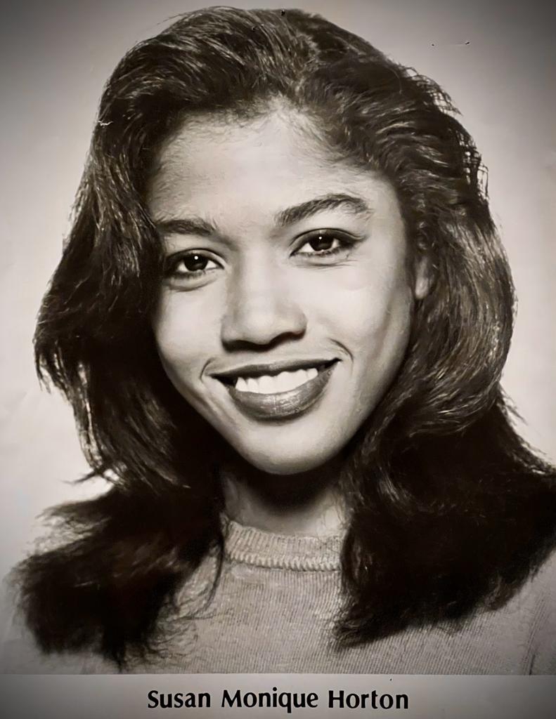 Black-and-white portrait of Susan Monique Horton smiling, with voluminous hair and casual attire.