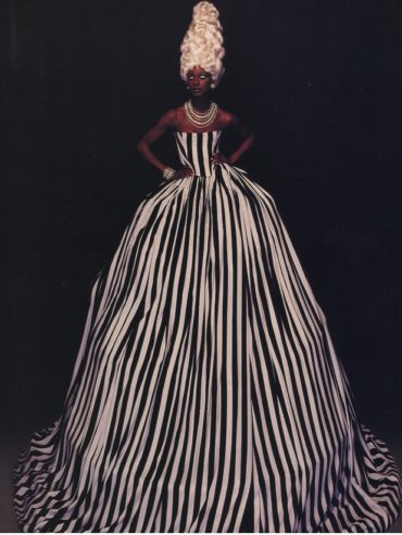 Woman in a dramatic black and white striped ball gown with elaborate jewelry and bold hairstyle.