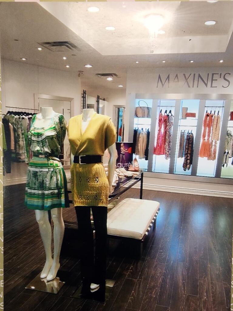 Mannequins display vibrant yellow and patterned green-and-white dresses in a boutique window.