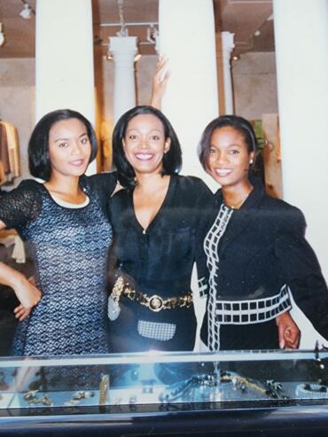 Three women standing together inside a boutique store, smiling and dressed in stylish black outfits.
