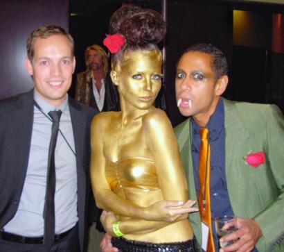 Three individuals at a social event, with one person painted gold and others dressed in stylish attire.