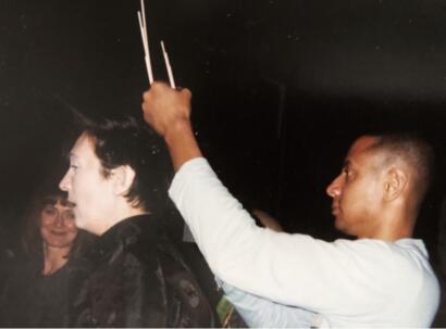 Person holding incense sticks over someone's head in a dimly lit setting.