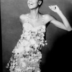 Black-and-white portrait of a woman smiling confidently in a sequined dress, raised arm.