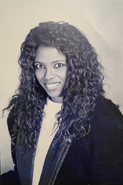 Black and white portrait of a woman with curly hair, smiling in a fashion magazine style.