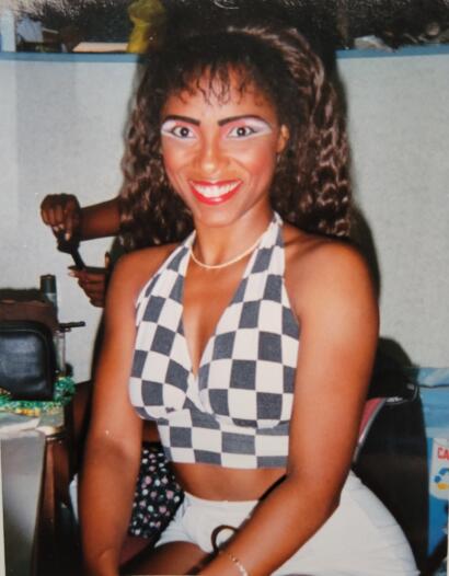 Woman with curly hair wearing a checkered halter top, smiling at the camera.