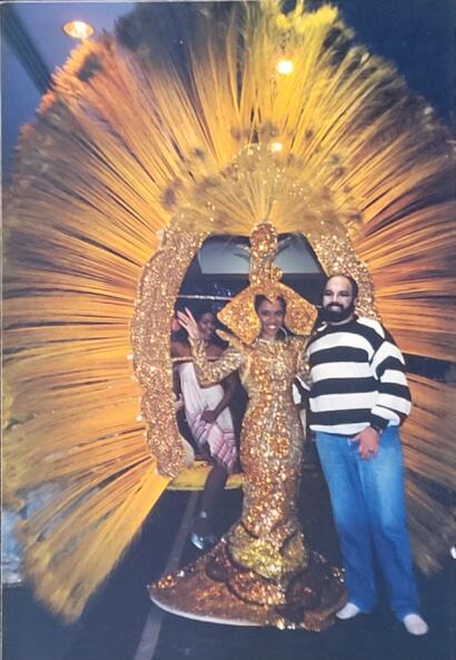 Three people pose with a gold, ornate, carnival-style headdress and costume.