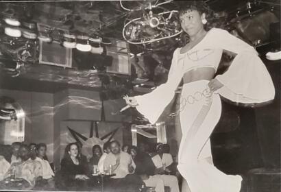 Woman in a flowing dress performing on stage at a lively entertainment venue.