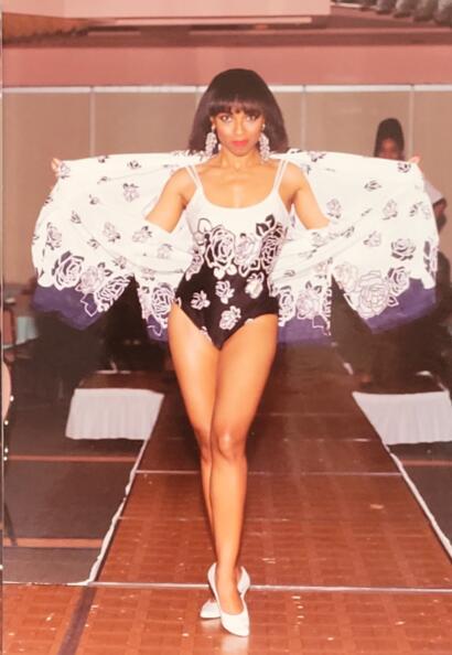 Model walking runway in a floral black-and-white fit-and-flare outfit with dramatic shoulder sleeves.