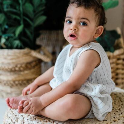 Baby boy seated on a woven mat, wearing a striped sleeveless outfit with a surprised expression.