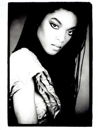 Black-and-white portrait of a woman with defined eyeliner, wearing a ruffled top, looking directly at the camera.