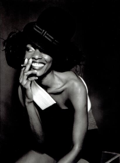 Black and white portrait of a smiling woman wearing a stylish hat, with a relaxed pose.