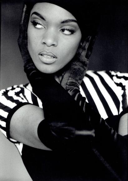 Black and white portrait of a woman with striking makeup, wearing striped top and elegant gloves.