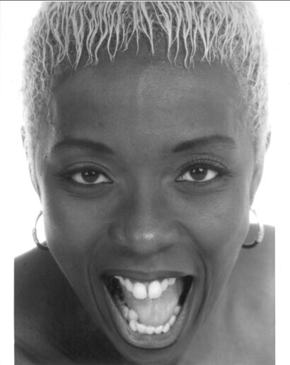 Close-up of a woman with short, platinum blonde hair, joyful expression, and hoop earrings.