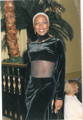 Woman with platinum short hair in black velvet outfit at an indoor event.