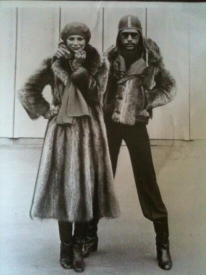 Black-and-white photo of a woman in a fur coat and hat, and a man in a leather jacket with fur accents, both dressed in vintage winter fashion.