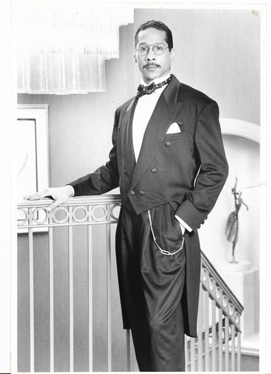 Man in vintage tuxedo with bow tie and pocket square, standing on staircase.