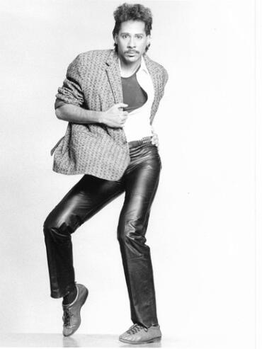 Black-and-white portrait of a man in a blazer, leather pants, and sneakers.