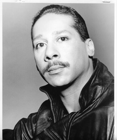 Black-and-white portrait of a man with a mustache, slicked-back hair, wearing a leather jacket.