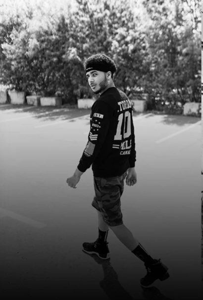 Young man in streetwear walking outdoors, with trees in background.