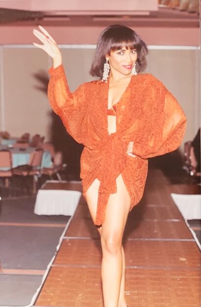 Model walking runway in orange patterned dress with dramatic puff sleeves, statement earrings.