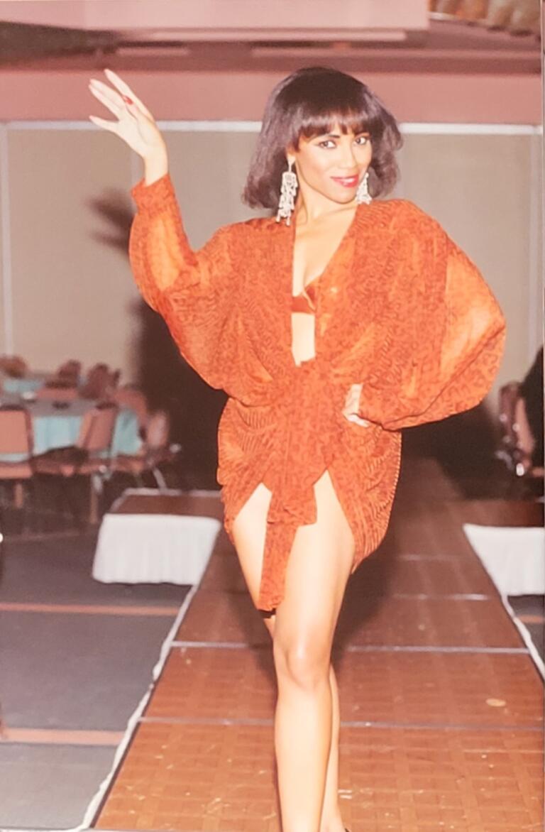 Model walking runway in orange patterned dress with dramatic puff sleeves, statement earrings.