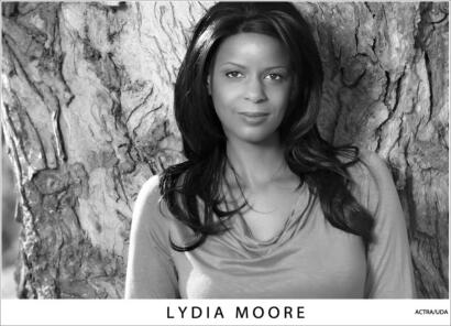 Portrait of Lydia Moore with natural hair, standing against a tree trunk.