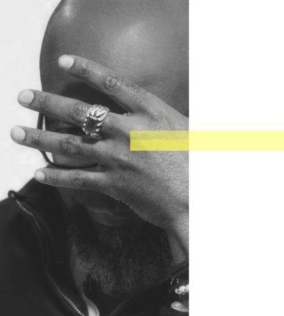 Close-up of a person with dark skin covering part of their face with their hand, wearing a ring and bracelet.