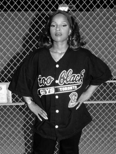 Stylish woman in a Toronto baseball jersey poses in front of a chain-link fence.