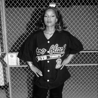 Stylish woman in a Toronto baseball jersey poses in front of a chain-link fence.