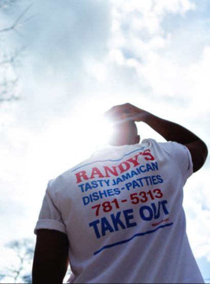Person wearing a white T-shirt with red and blue text, taken outdoors against a cloudy sky.