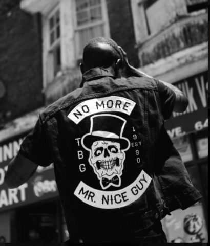 Back view of a man wearing a patch-covered denim jacket with skull design, on an urban street in black and white.