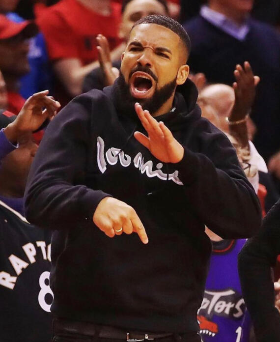 A man passionately gestures and shouts during a sports event, surrounded by cheering spectators.