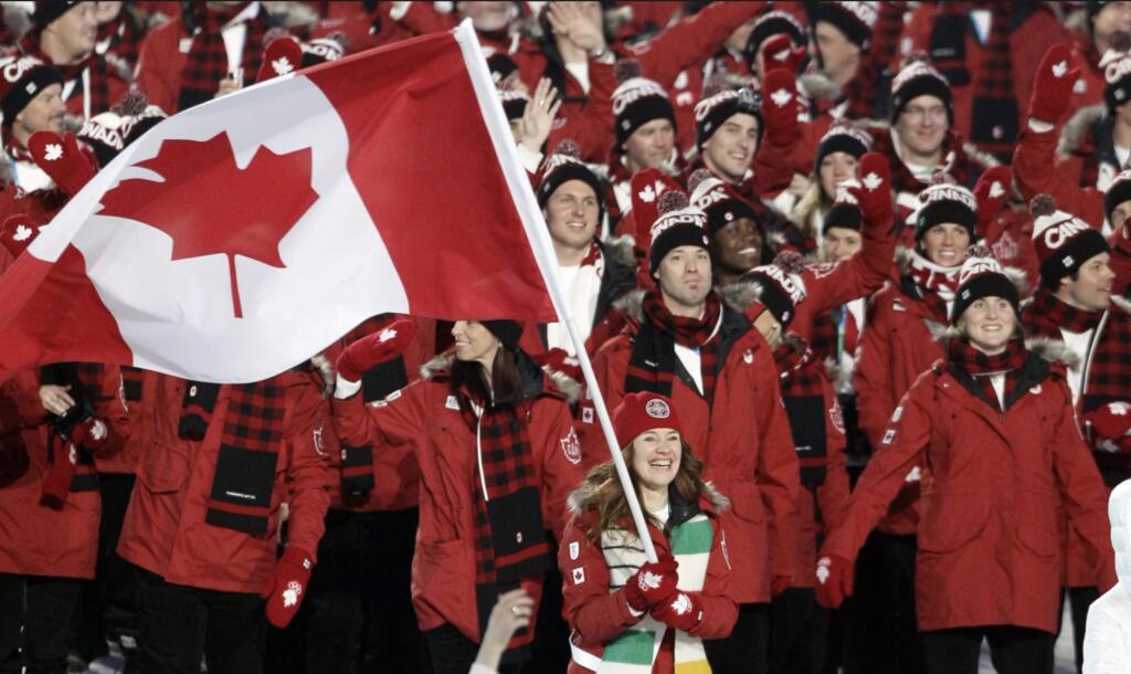 Canadian Olympic team cheerfully waving a maple leaf flag at a winter event.