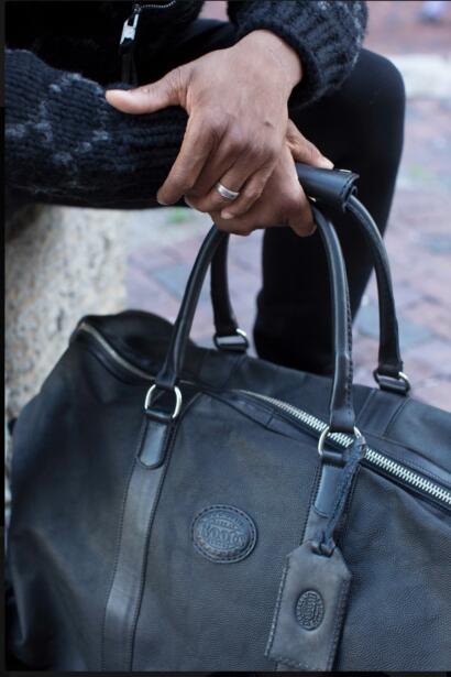 Close-up of hands with rings holding a black leather bag with silver zippers.
