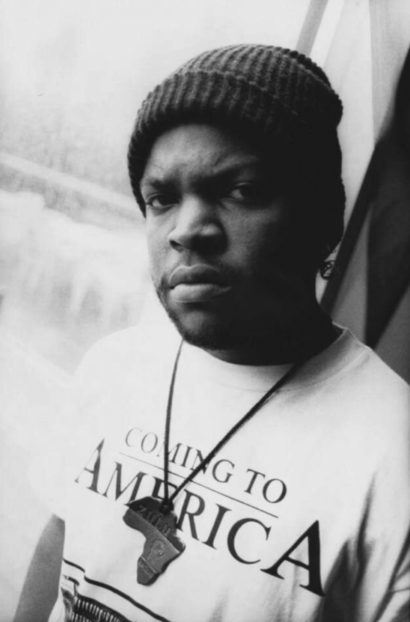 Portrait of a man wearing a beanie and a "Coming to America" t-shirt, captured in black and white.