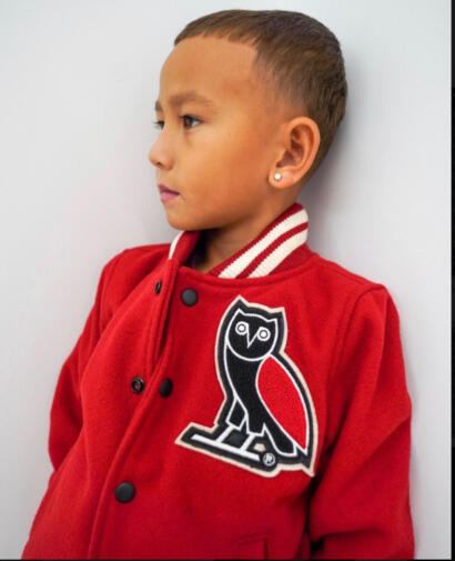 Young boy in a red varsity jacket with an owl patch, against a plain wall.