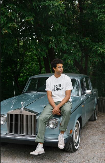 Man sitting on classic Rolls-Royce car, wearing casual white T-shirt and olive green pants.