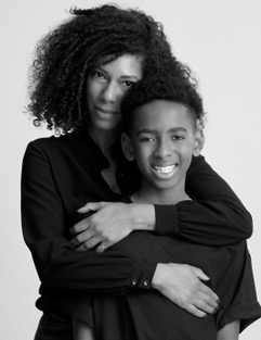 Mother and daughter embracing, both with natural curly hair, in black attire.