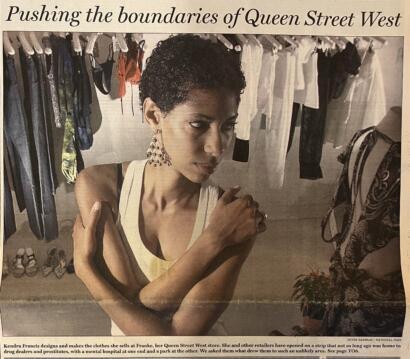A woman with short curly hair wearing earrings, posing among clothing racks at a boutique.