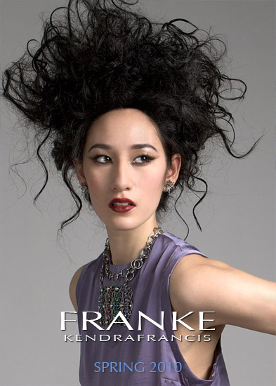 Model with voluminous curly hair wearing lilac satin top, accessorized with layered jewelry.