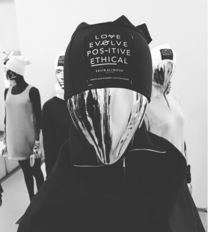Mannequin with metallic face mask wearing a black headwear with philosophical quotes, in a fashion display.