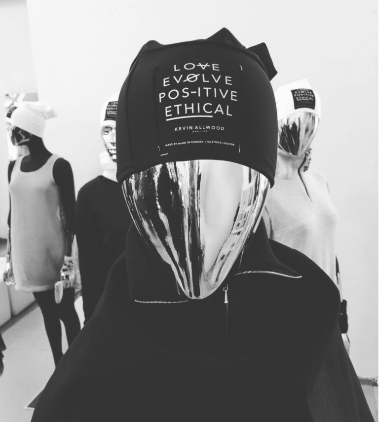Mannequin with metallic face mask wearing a black headwear with philosophical quotes, in a fashion display.